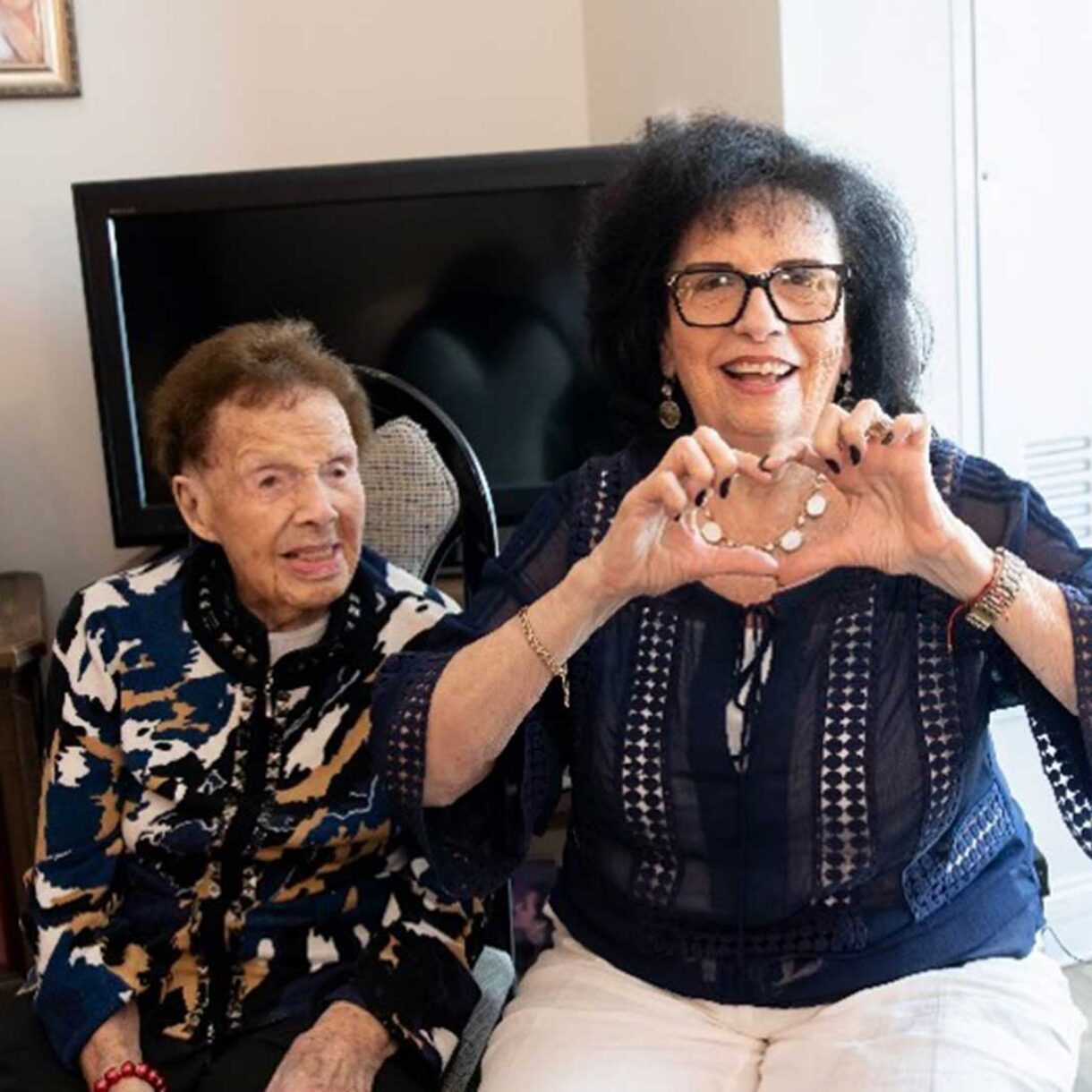 Holocaust Survivor sits on a chair with a volunteer